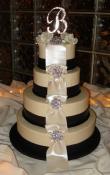 Candlelight buttercream iced wedding cake, with wide fondant ribbons and pearlescent bow loops cascading from the top tier to the bottom. Brooches are used as an accent instead of flowers but are mixed together with the monogram topper. 